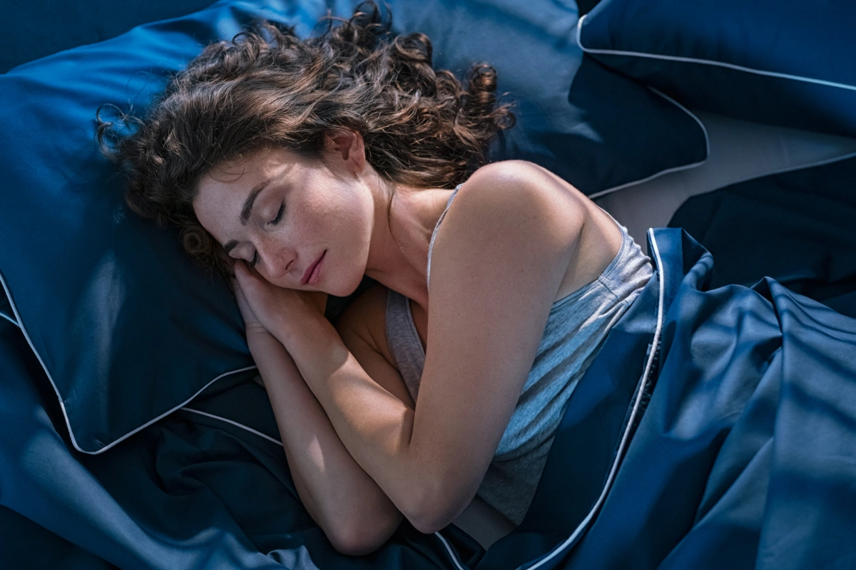 Woman sleeping peacefully in blue bedding, head resting on pillow.