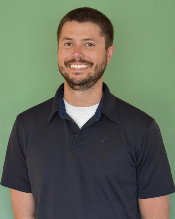 Professional headshot of smiling man in dark polo shirt against green background.