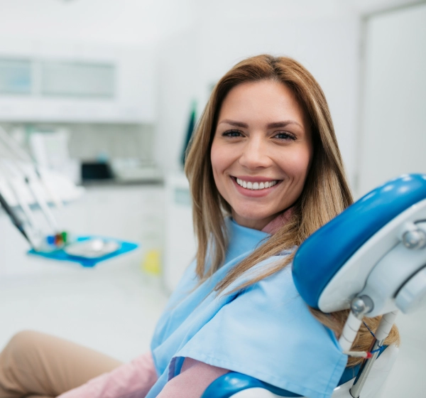 Female dentist smiling in modern dental office with equipment visible in background.