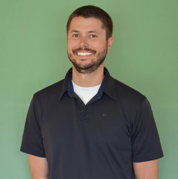 Man in dark polo shirt smiling against green background for dental practice headshot.