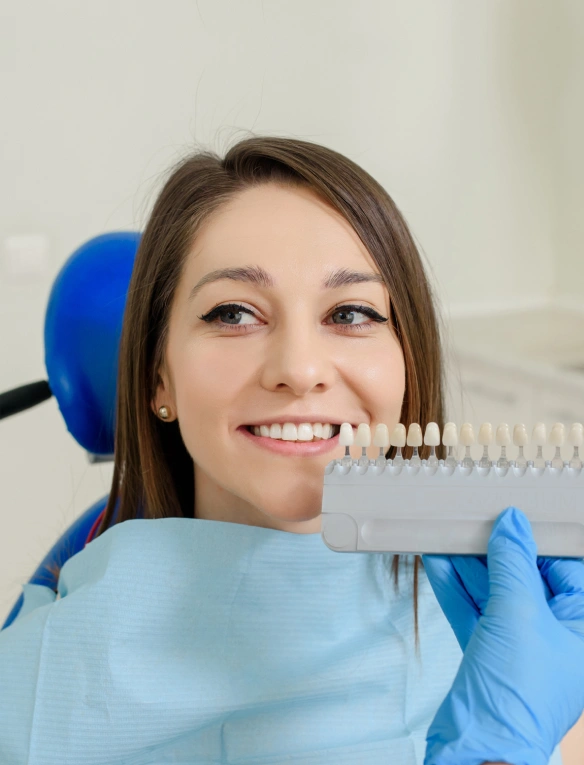 Dental professional holding teeth shade guide in modern dental office setting, smiling at camera.