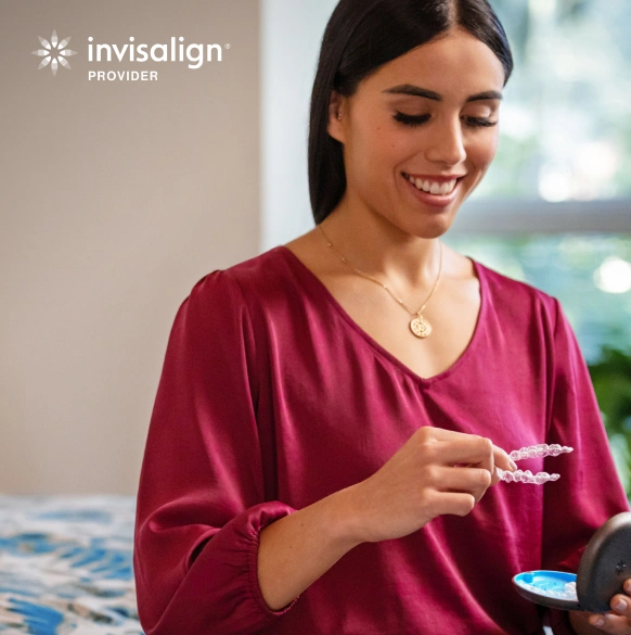 Woman holding Invisalign aligners in dental office setting, smiling at clear braces.