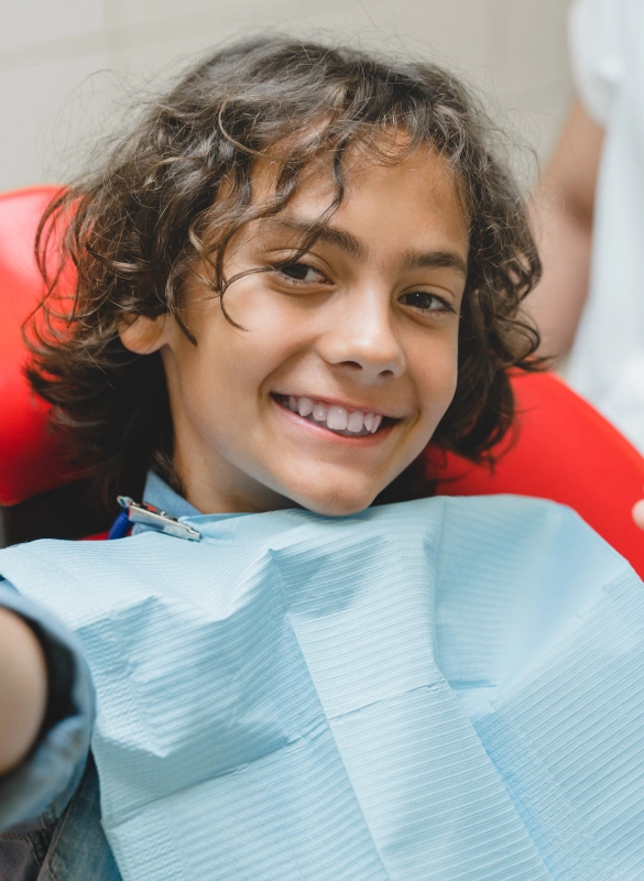 Young child smiling in dental chair wearing bib at Parker Dentistry office